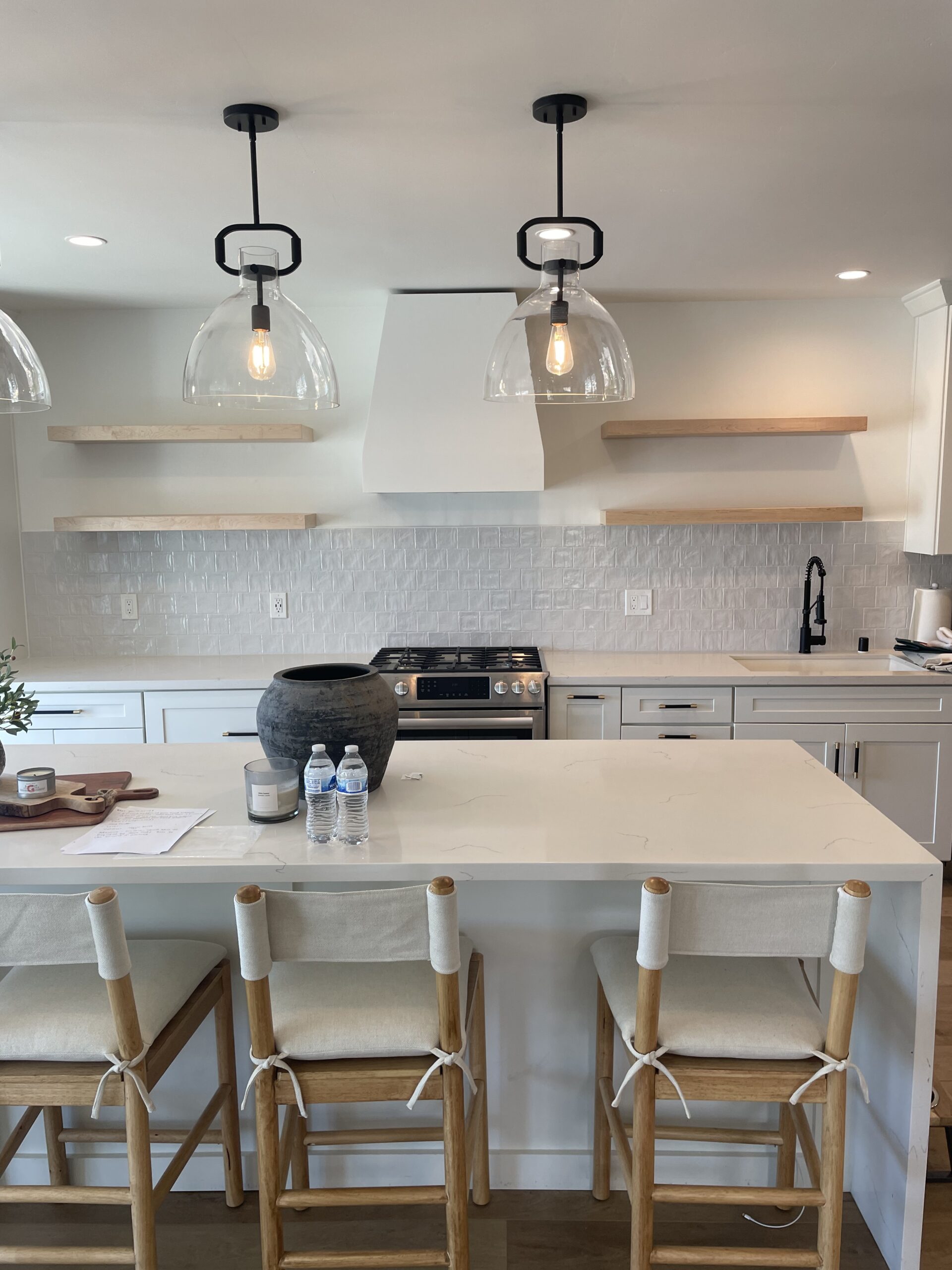 A beautifully remodeled white kitchen with clean and bright White Island countertop as well as white cabinets in the kitchen. Modern, wooden high chairs along with the white countertop.