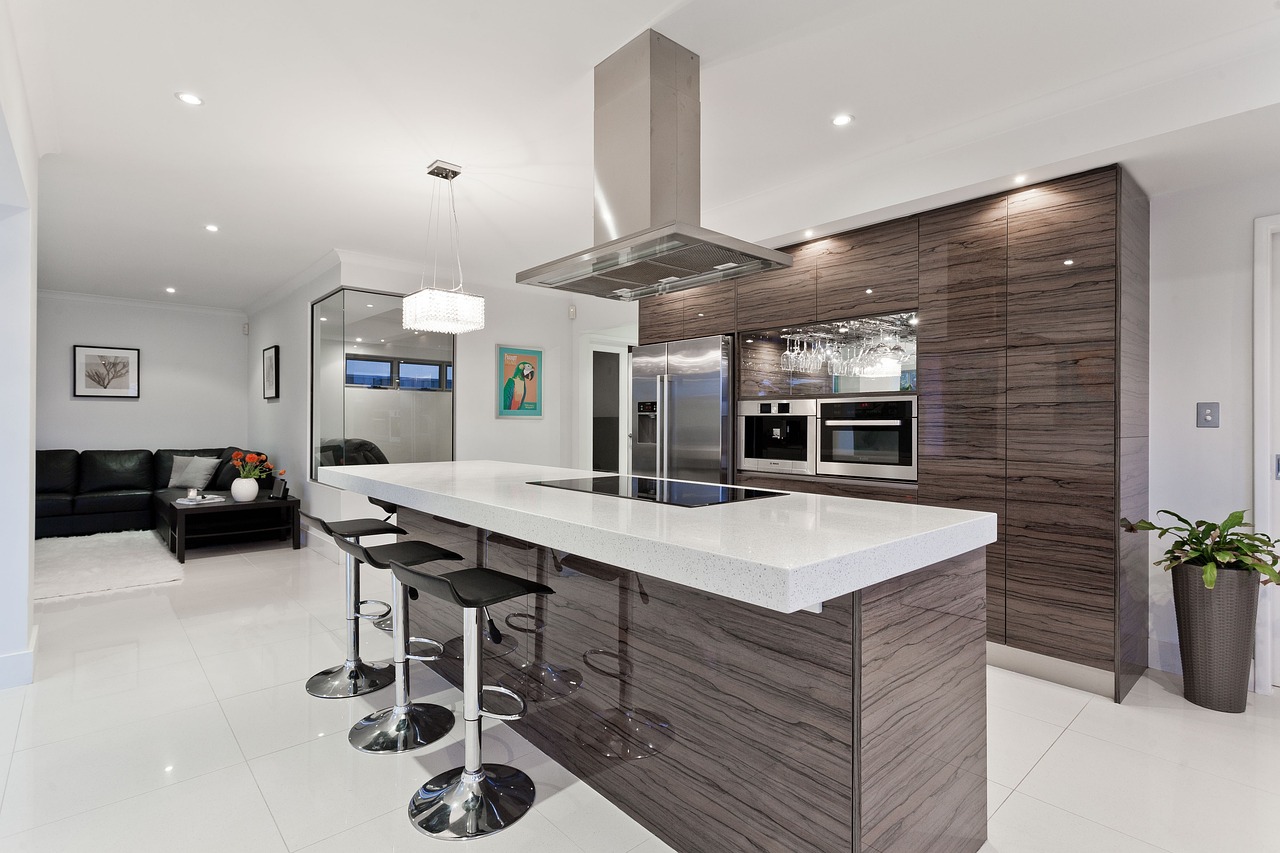 kitchen, interior design, house-1809844.jpg car while flooring with brown wood on all cabinetry, walls and body of the island. Clean white stone for the countertop on the island with an electric stovetop at the middle of the island with a silver ventilator over it.