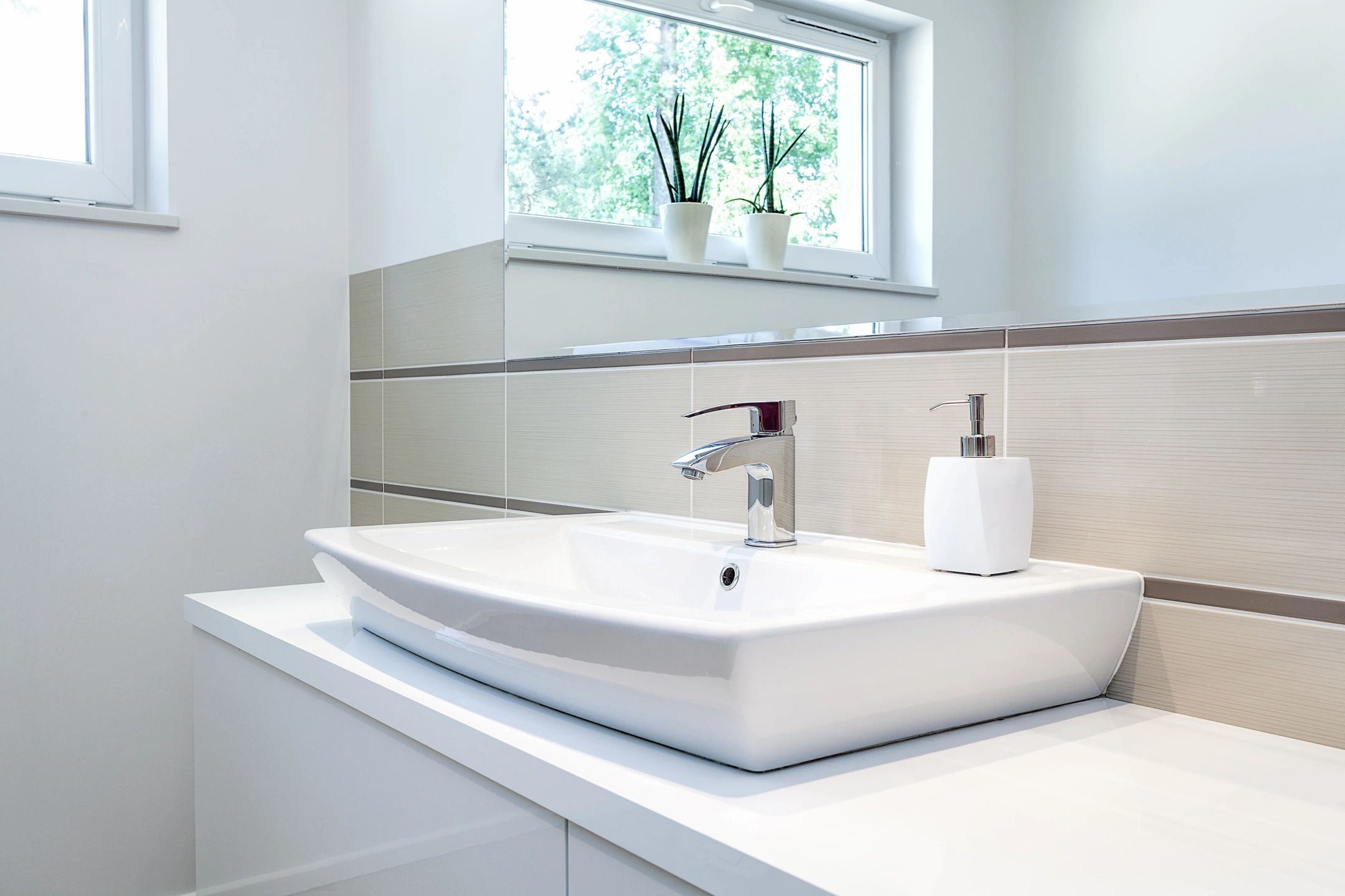 close up of white stone bathroom sink with silver nozzle. White Sabin under the sink and large bathroom mirror.