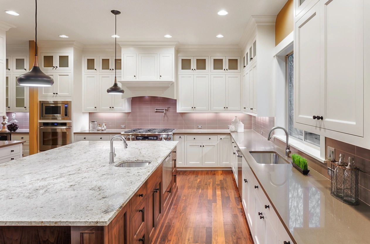 White kitchen cabinets with classy stone marble counters. Dark brown hardwood flooring in the kitchen with the same wood for the body of the island.